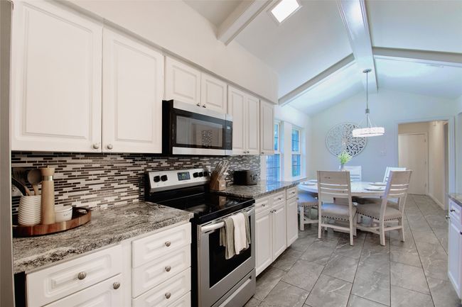 Kitchen featuring stainless steel appliances, tasteful backsplash, white cabinets, a chandelier, and hanging light fixtures | Image 14