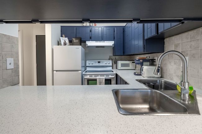 Kitchen featuring a sink, white appliances, under cabinet range hood, decorative backsplash, and blue cabinets | Image 13