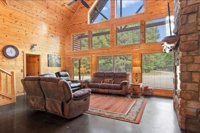 Living area with high vaulted ceiling, a ceiling fan, wooden walls, finished concrete floors, and stairway | Image 7