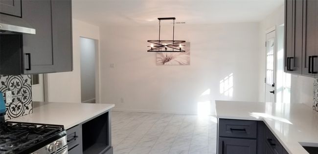 Kitchen with a chandelier, exhaust hood, light countertops, light marble finish floors, and decorative light fixtures | Image 15