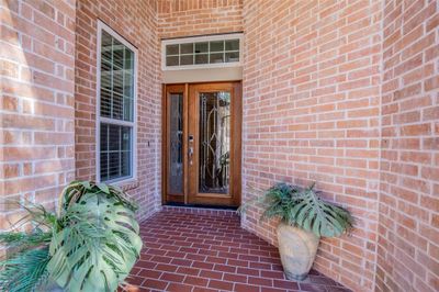 This is a welcoming entryway featuring beautiful front door with side windows and transom, complemented by warm red brick walls and a herringbone patterned tile porch. | Image 2