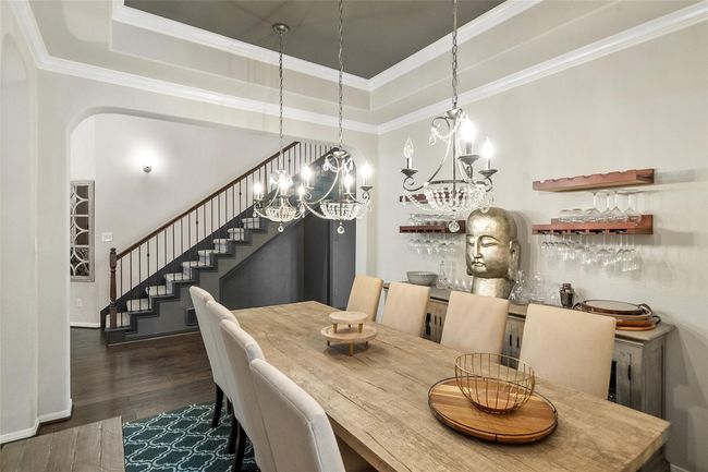 This elegant dining room features a striking chandelier. The space is accented by a modern staircase. | Image 14