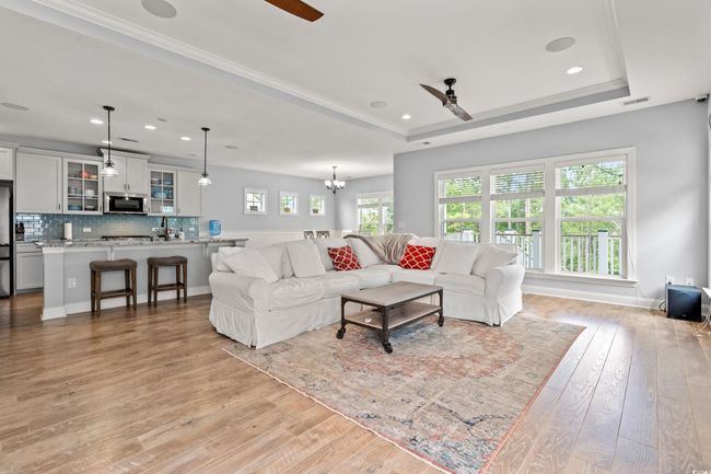Living room with ceiling fan, light wood-type flooring, a tray ceiling, recessed lighting, and a chandelier | Image 4