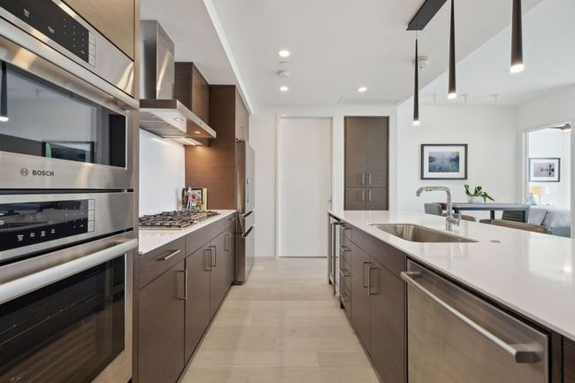 Kitchen featuring appliances with stainless steel finishes, a sink, light countertops, wall chimney exhaust hood, and dark brown cabinetry | Image 18