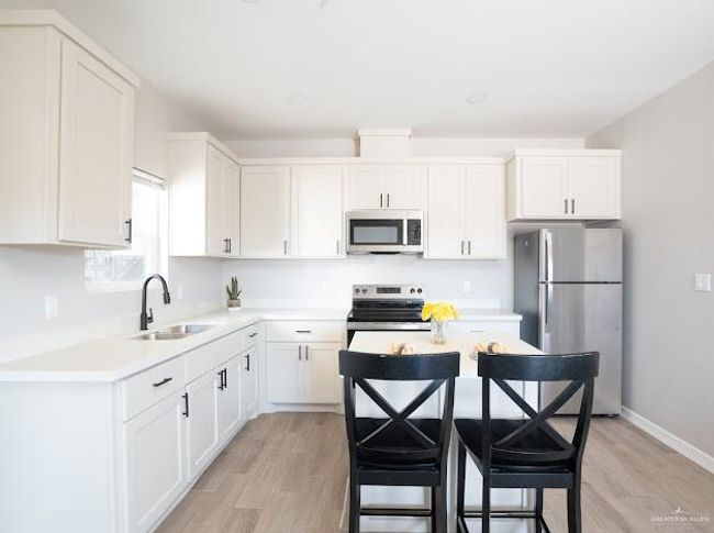 Kitchen with appliances with stainless steel finishes, sink, white cabinets, a kitchen breakfast bar, and light hardwood / wood-style floors | Image 6