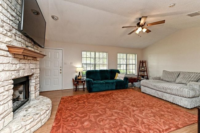 Living area with vaulted ceiling, wood finished floors, a stone fireplace and ceiling fan. Great Windows for Natural Light | Image 4