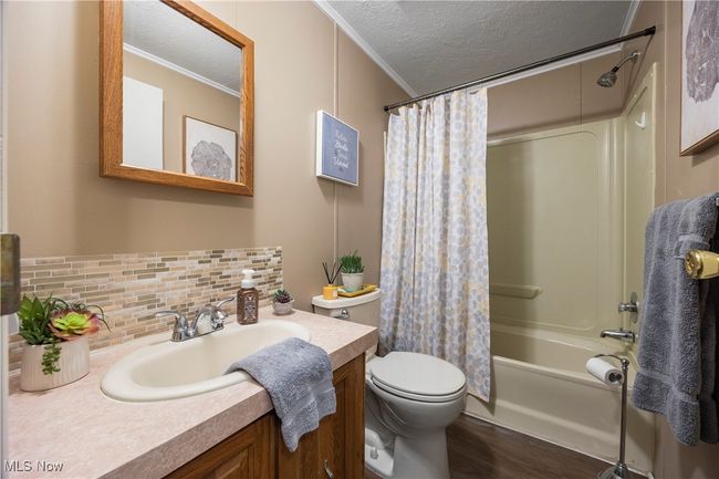 Full bath featuring crown molding, vanity, wood finished floors, a textured ceiling, and shower / bathtub combination with curtain | Image 33