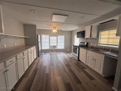 Kitchen with dark wood-type flooring, stainless steel appliances, ceiling fan, white cabinetry, and tasteful backsplash | Image 3