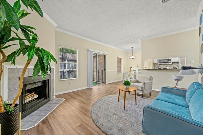 Living room with light wood-style floors, ornamental molding, a tile fireplace, a textured ceiling, and baseboards | Image 8