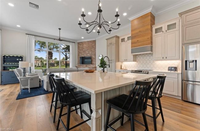 Kitchen with appliances with stainless steel finishes, a kitchen island with sink, light countertops, crown molding, and light wood-type flooring | Image 7