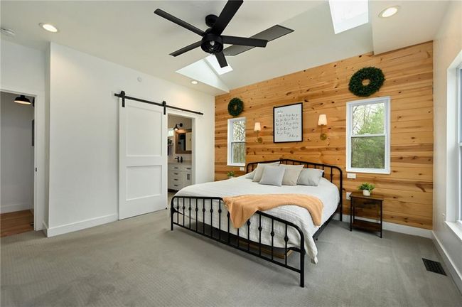 Bedroom featuring two skylight, a barn door, wood accent wall, light carpet. A television is hung cleverly above the bed. | Image 26