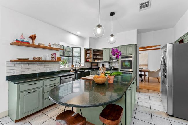 Kitchen with green cabinets, open shelves, stainless steel appliances, backsplash, and light tile patterned flooring | Image 13