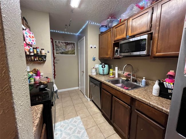 Kitchen featuring appliances with stainless steel finishes, light tile patterned floors, a textured ceiling, and light countertops | Image 6