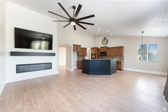 Great room featuring a vaulted ceiling, a ceiling fan, arched walkways, a large fireplace, and light wood-style flooring | Image 11