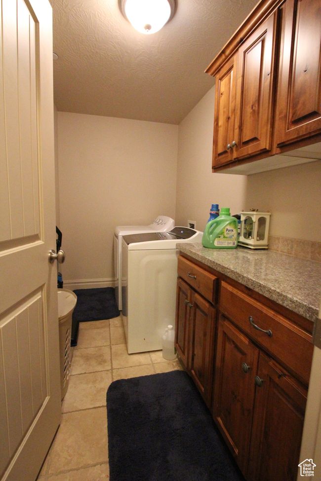 Laundry area with a textured ceiling, light tile patterned floors, washing machine and dryer, baseboards, and cabinet space | Image 9