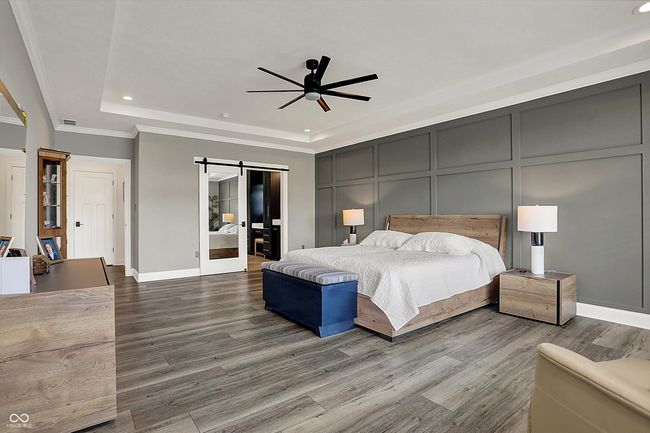 bedroom featuring a barn door, recessed lighting, a tray ceiling, wood finished floors, and a decorative wall | Image 24