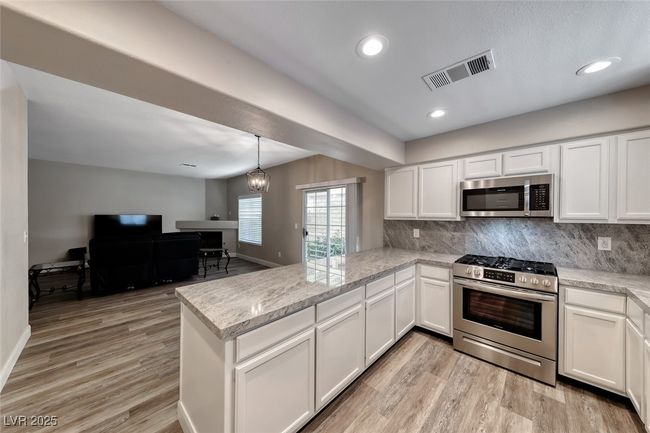 Kitchen featuring stainless steel appliances, a peninsula, white cabinetry, tasteful backsplash, and light wood finished floors | Image 12