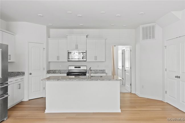 Kitchen featuring white cabinets, a sink, a kitchen island with sink, stainless steel appliances, and visible vents | Image 6