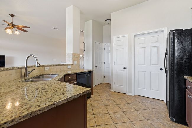 Kitchen featuring a sink, light tile patterned flooring, a ceiling fan, light stone countertops, and black appliances | Image 14