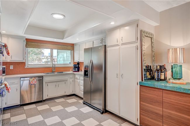 Kitchen featuring a tray ceiling, light floors, appliances with stainless steel finishes, white cabinetry, and a sink | Image 17