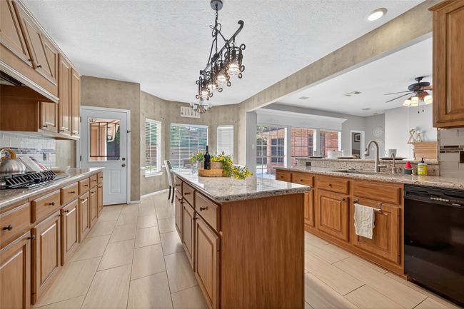 This spacious kitchen features warm wood cabinetry, granite countertops, and a central island. It opens to a bright dining area with large windows and access to a patio, creating a perfect blend of indoor and outdoor living. | Image 11