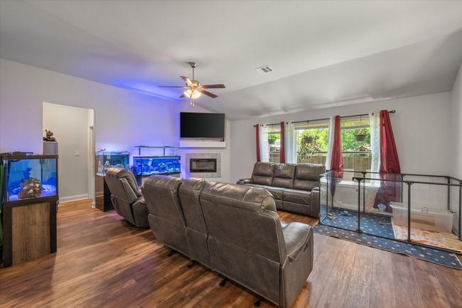 Living room with wood finished floors, ceiling fan, vaulted ceiling, and an electric fireplace. | Image 6