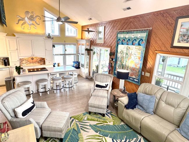 Living room with a ceiling fan, wood walls, light wood-type flooring, and high vaulted ceiling | Image 22