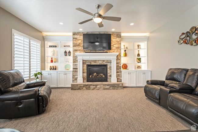 Carpeted living area featuring ceiling fan, a stone fireplace, recessed lighting, and built in features | Image 13