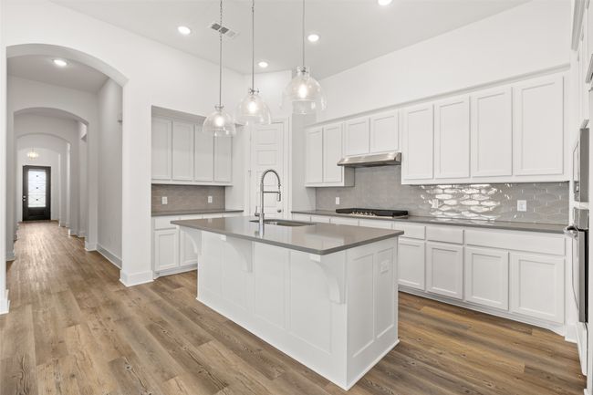 Kitchen featuring under cabinet range hood, a sink, arched walkways, stainless steel gas stovetop, and wood finished floors | Image 18