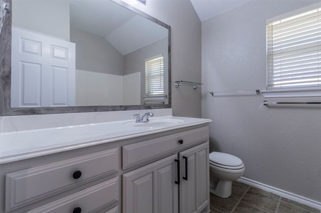 Bathroom with lofted ceiling, tile patterned flooring, a textured wall, toilet, and vanity | Image 23