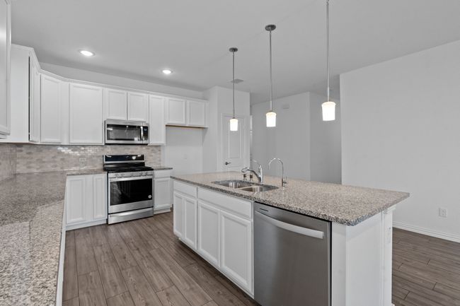 Kitchen featuring appliances with stainless steel finishes, tasteful backsplash, dark wood-type flooring, white cabinetry, and light stone countertops | Image 8