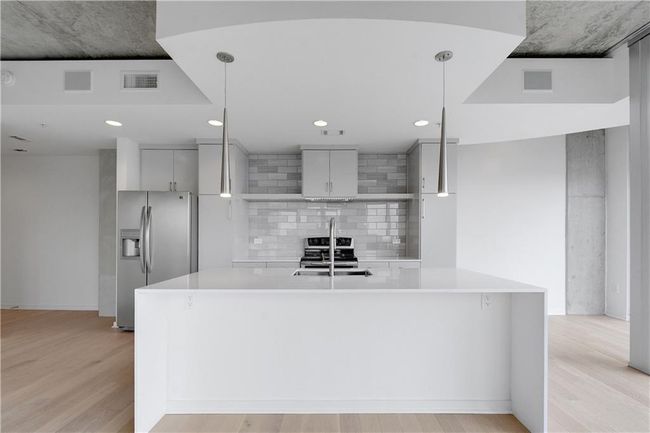Kitchen featuring light countertops, light wood-style flooring, stainless steel fridge, a sink, and backsplash | Image 4