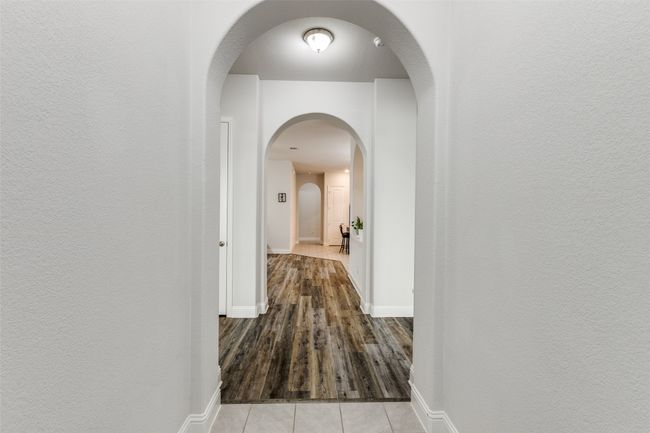 Corridor with light tile patterned flooring, a textured wall, and baseboards | Image 4