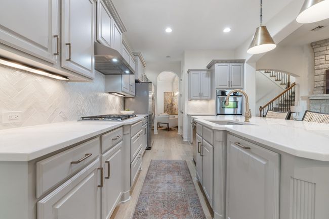 Kitchen featuring arched walkways, appliances with stainless steel finishes, range hood, a sink, and decorative backsplash | Image 9