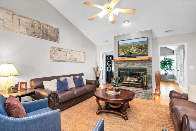 Living room featuring a ceiling fan, wood finished floors, a fireplace, and lofted ceiling | Image 8