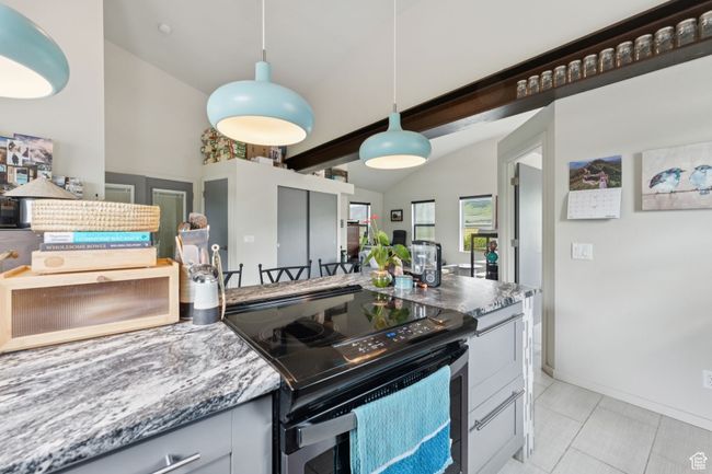 Kitchen featuring black / electric stove, vaulted ceiling, pendant lighting, light tile patterned floors, and stone counters | Image 34