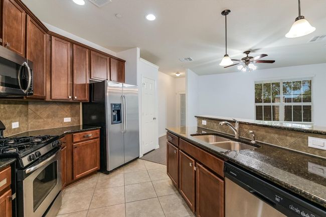 Kitchen with stainless steel appliances, decorative backsplash, pendant lighting, light tile patterned flooring, and dark stone countertops | Image 9