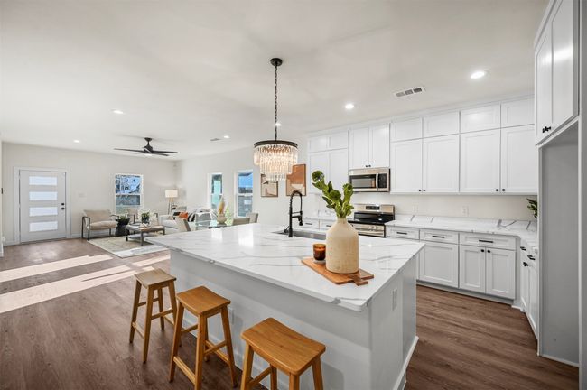 Kitchen featuring light stone countertops, stainless steel appliances, white cabinets, a sink, and visible vents | Image 12