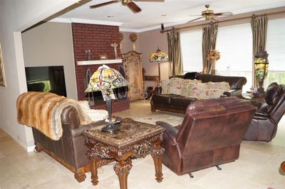 Tiled living room featuring crown molding, a brick fireplace, brick wall, and ceiling fan | Image 2