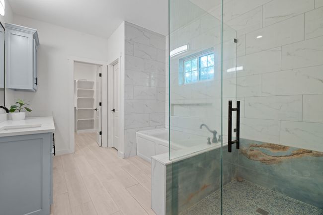 Full bath featuring a shower stall, vanity, a bath, a walk in closet, and wood finished floors | Image 24