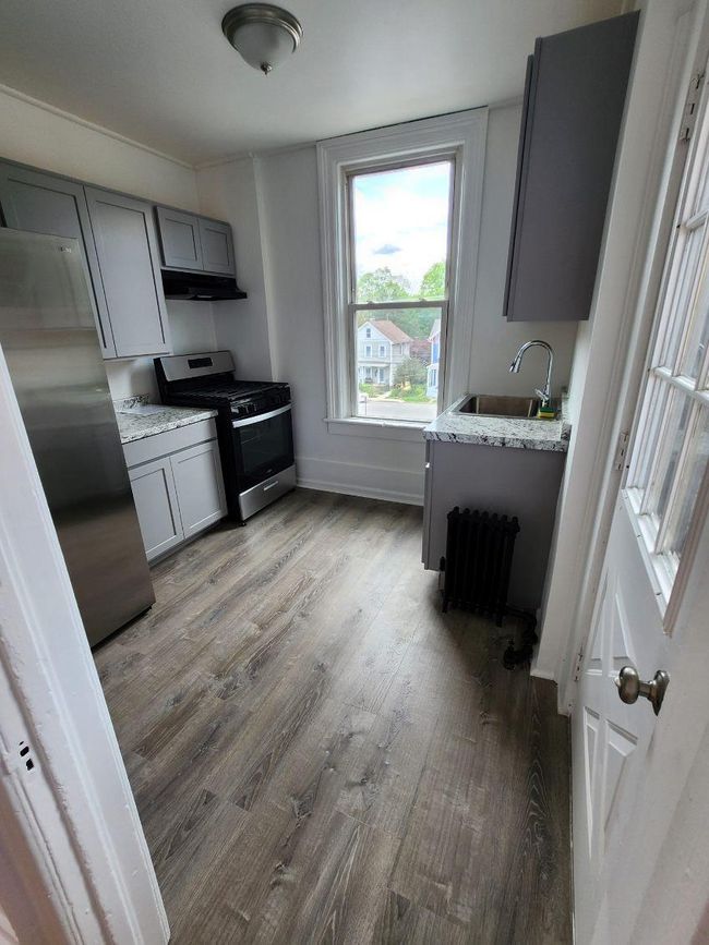 Newly renovated kitchen with a sink, appliances with stainless steel finishes, gray cabinets, and radiator heating unit | Image 4