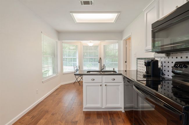 Kitchen featuring black appliances, a peninsula, dark countertops, backsplash, and white cabinetry | Image 15