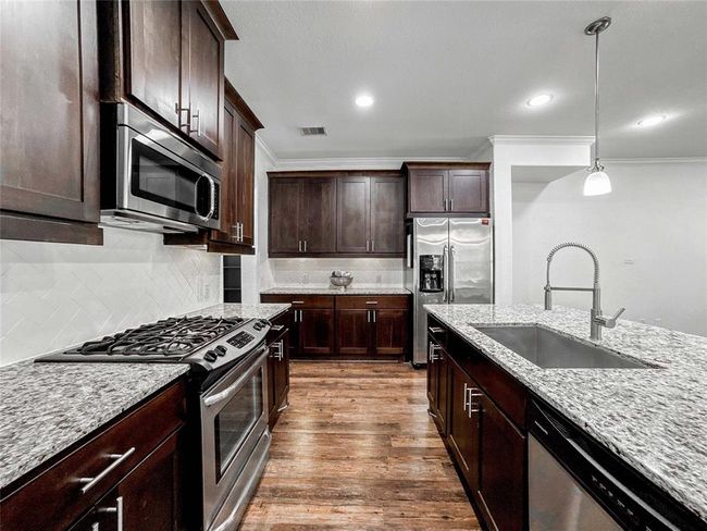 This modern kitchen features rich dark wood cabinets, granite countertops, and stainless steel appliances. It includes a spacious island with a built-in sink, a 4 burner gas stove, and ample storage, creating an inviting space for cooking and entertaining. | Image 9