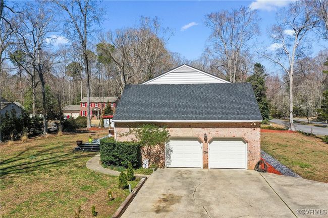 View of side of property featuring driveway, roof with shingles, an attached garage, a lawn, and brick siding | Image 41