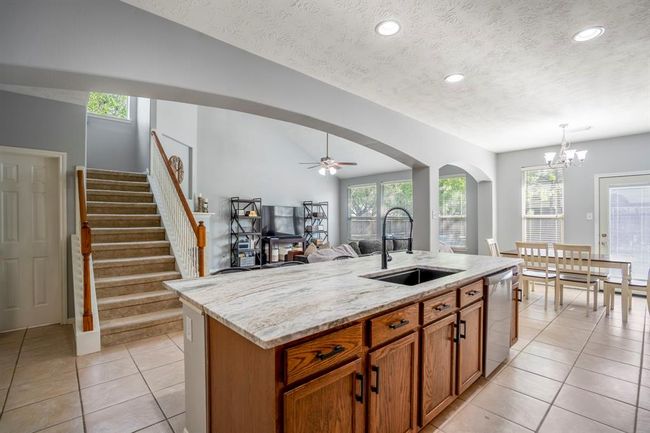 Looking out across the island, you’ll notice generous storage space beneath the countertop, a view of the living room framed by dramatic archways, and the nearby breakfast area. Just to the left of the stairs is the doorway to the half bath, which also leads to a spacious understairs closet. | Image 12