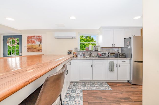 Kitchen featuring a wall mounted air conditioner, freestanding refrigerator, recessed lighting, wood finished floors, and white cabinets | Image 14