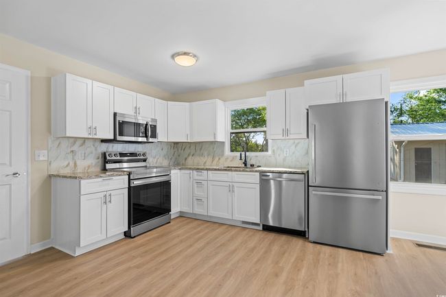Kitchen featuring appliances with stainless steel finishes, light wood-type flooring, white cabinets, light stone countertops, and tasteful backsplash | Image 19