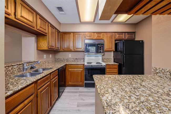 Kitchen featuring a sink, black appliances, light wood finished floors, light stone countertops, and visible vents | Image 4
