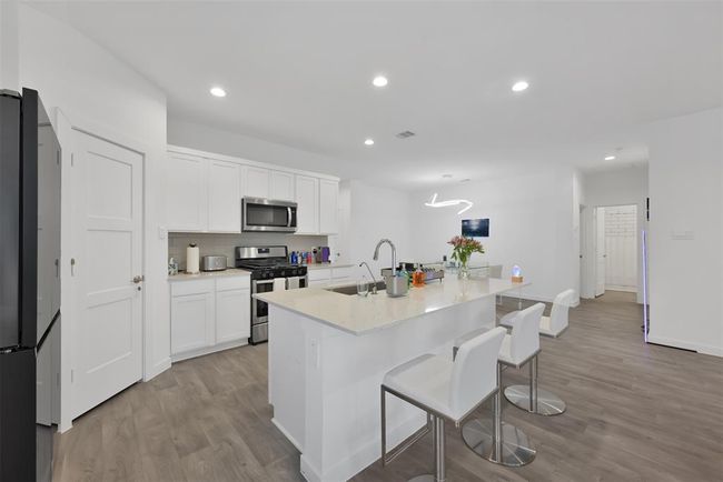 Modern kitchen with sleek white cabinetry, stainless steel appliances, and a spacious island with seating. Bright, open layout with wood flooring and contemporary lighting. Perfect for entertaining. | Image 9