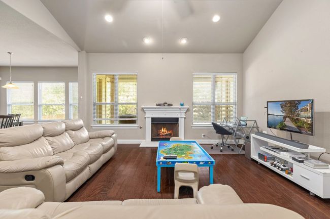 Living room with lofted ceiling, wood finished floors, a warm lit fireplace, and recessed lighting | Image 8
